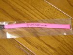 A pink phone strap with black text reading "ayumi hamasaki" in the same font used for the A single. It is wrapped in plastic and sitting on a wooden surface.